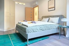 A bedroom with a bed, bedside table, lamp, and a door with a window. - MidTerm - Rooftop Serenity Apartment 2 (Budapest)