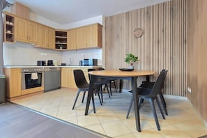 A modern kitchen with wooden cabinets, a built-in oven, and a dining area with a round table and chairs. - MidTerm - Rooftop Serenity Apartment 2 (Budapest)