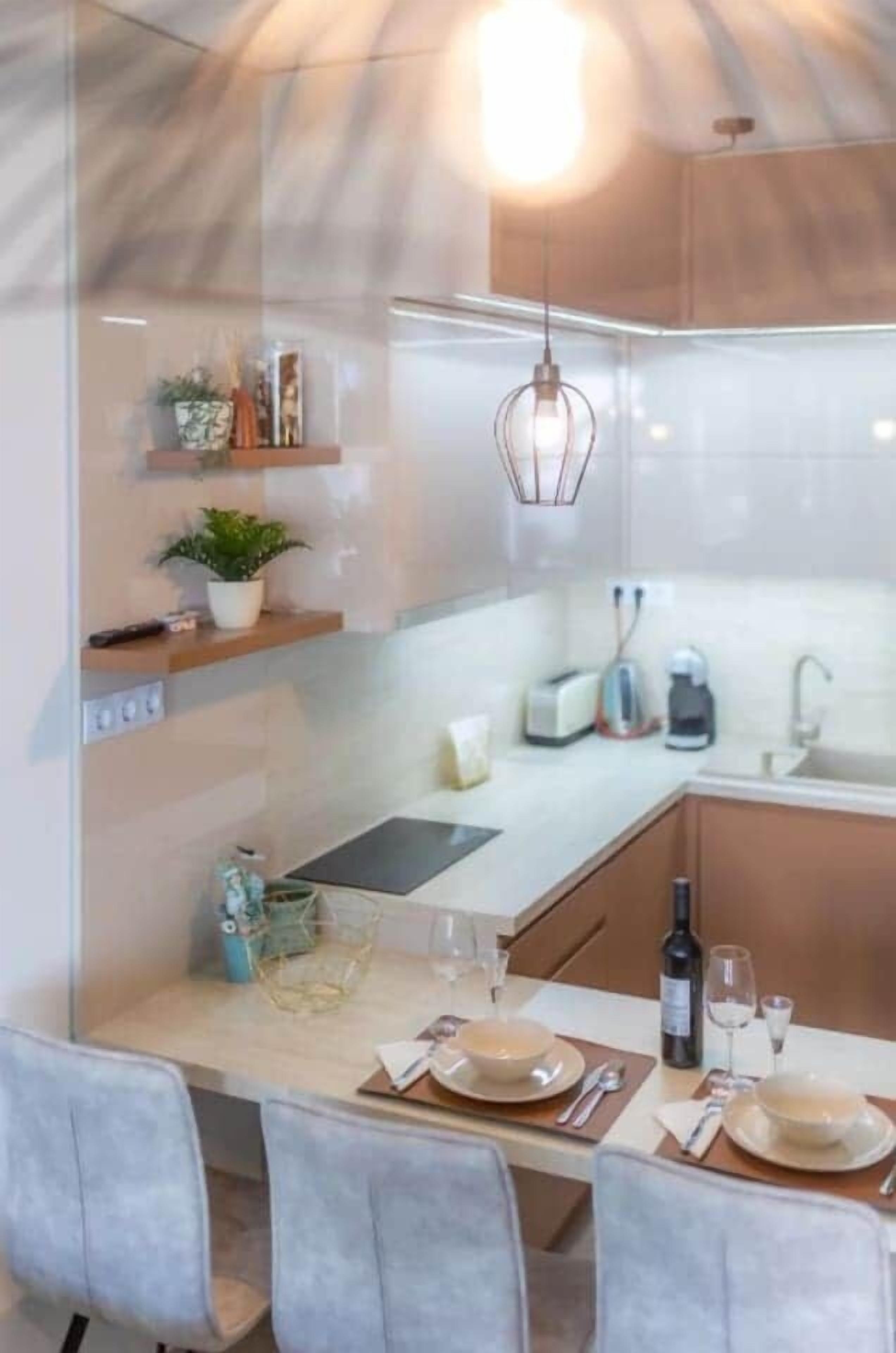 Una cocina moderna con comedor, que presenta un separador de vidrio, armarios de madera, una lámpara colgante y una mesa preparada para dos personas.