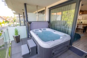 Ein Whirlpool auf einem Balkon mit Glastrennwand, einer kleinen Sitzecke und einem Blumentopf.