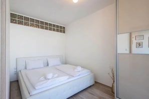 Ein Schlafzimmer mit einem Bett, einem Fenster mit Jalousien und einem an der Wand befestigten Regal.