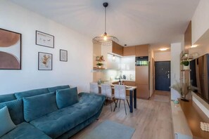Ein modernes Wohnzimmer mit Sofa, Essbereich, Küche und einem großen Fenster.