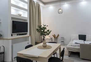 A modern living room with a flat-screen TV, a dining table with chairs, a sofa, and a bed. - MidTerm - Magpie Apartment (Budapest)