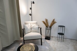 A modern living room with a light grey armchair, a floor lamp, a small black side table, and a decorative vase with pampas grass. - MidTerm - Magpie Apartment (Budapest)