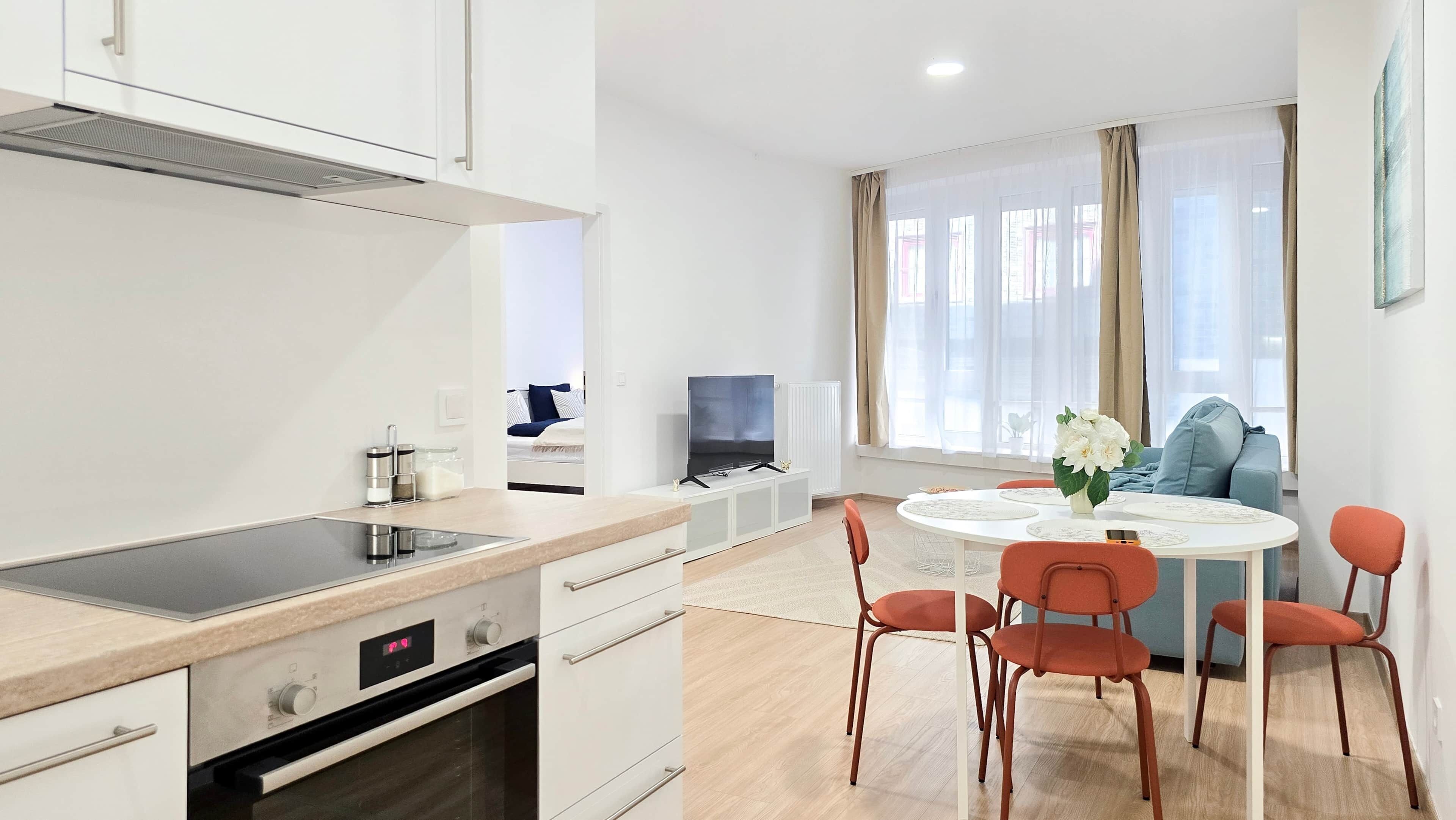 Une cuisine moderne dotée d’une cuisinière intégrée, un coin repas avec une table ronde et des chaises, et un téléviseur en arrière-plan.