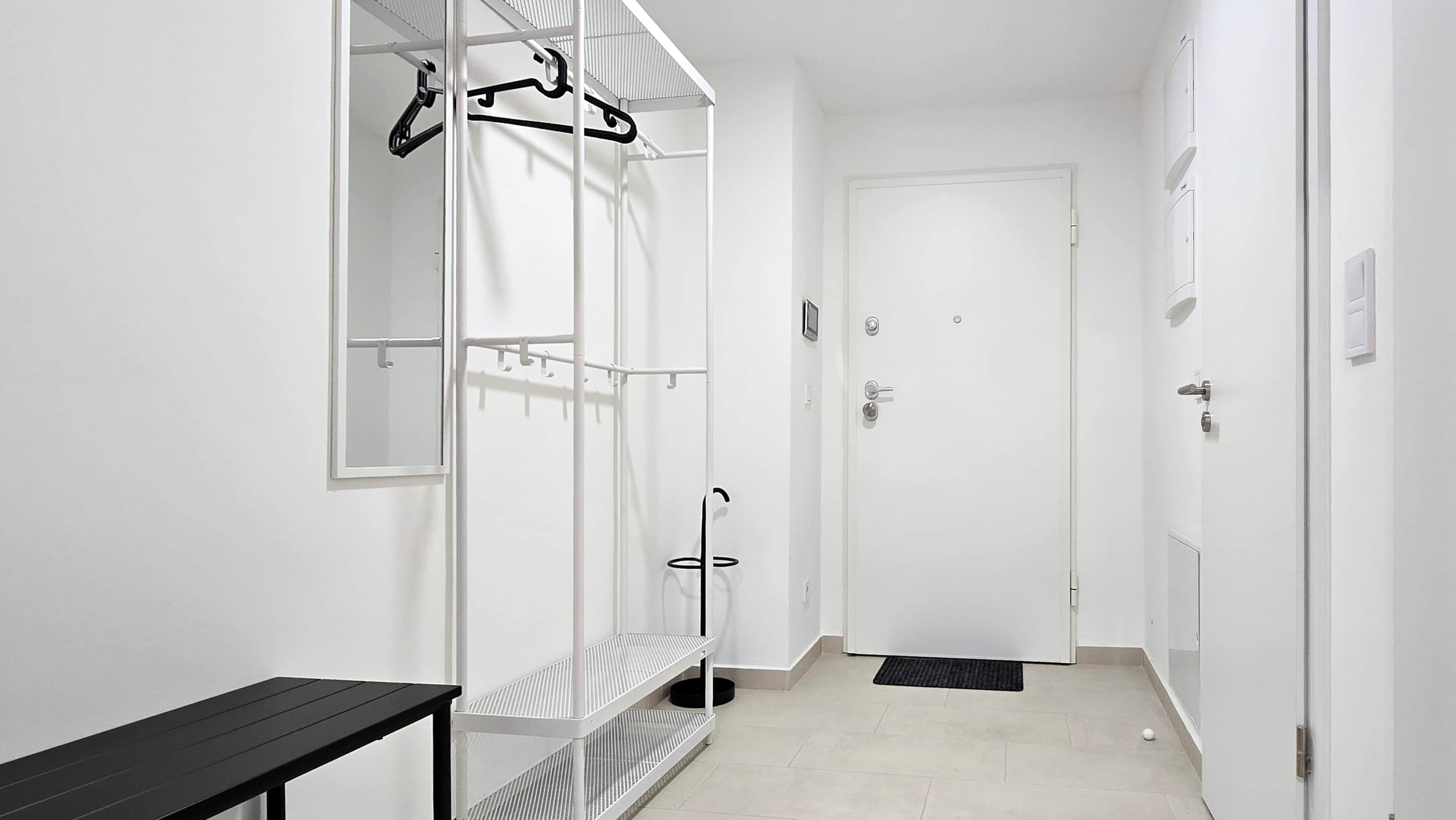 Un couloir étroit avec une porte blanche, un porte-manteau et une petite table.