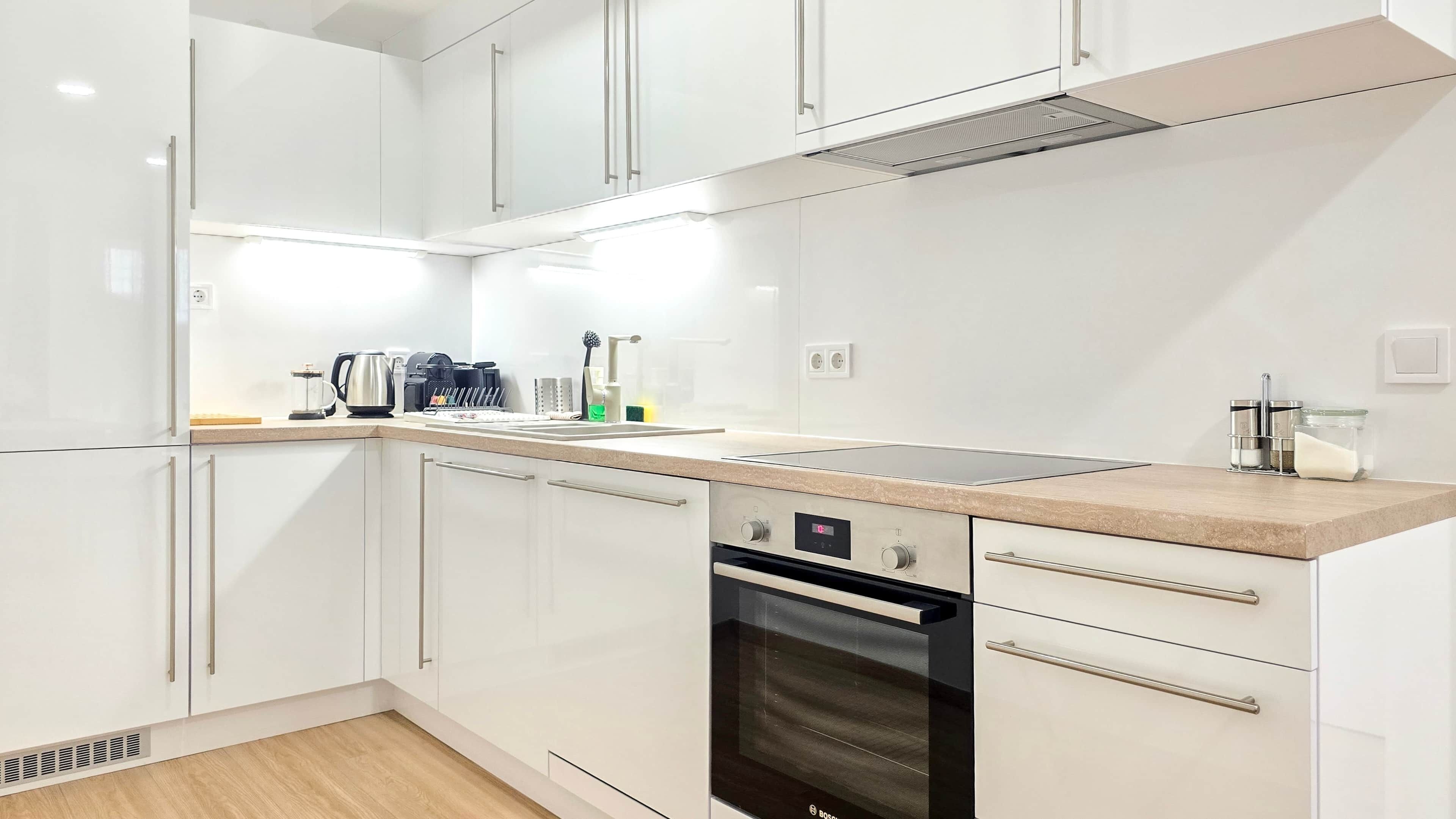 A modern kitchen with white cabinets, a built-in oven, and a stainless steel range hood.
