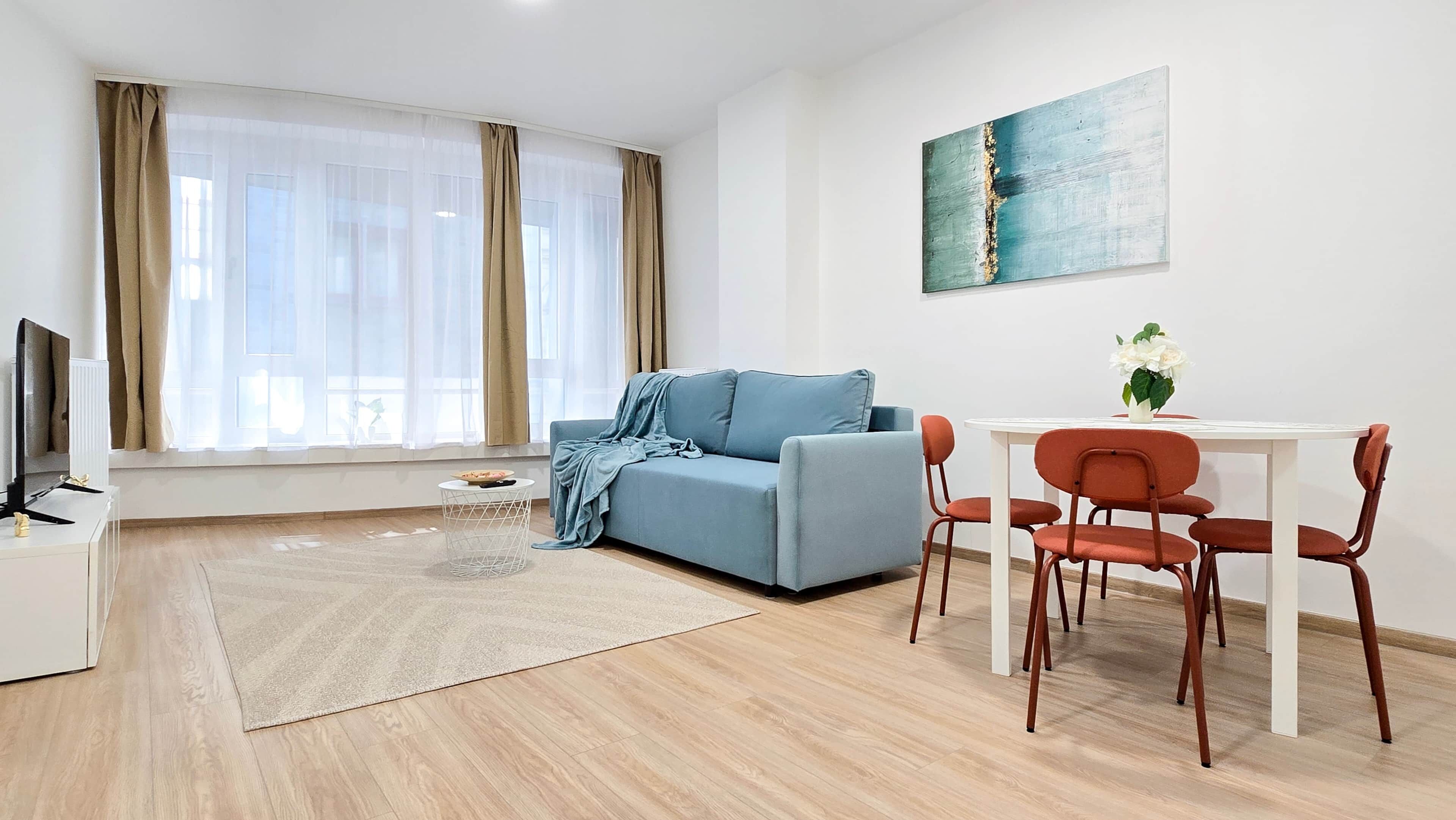 Ein modernes Wohnzimmer mit einer Couch, einem Esstisch mit Stühlen, einem Fernseher und einem Bild an der Wand.