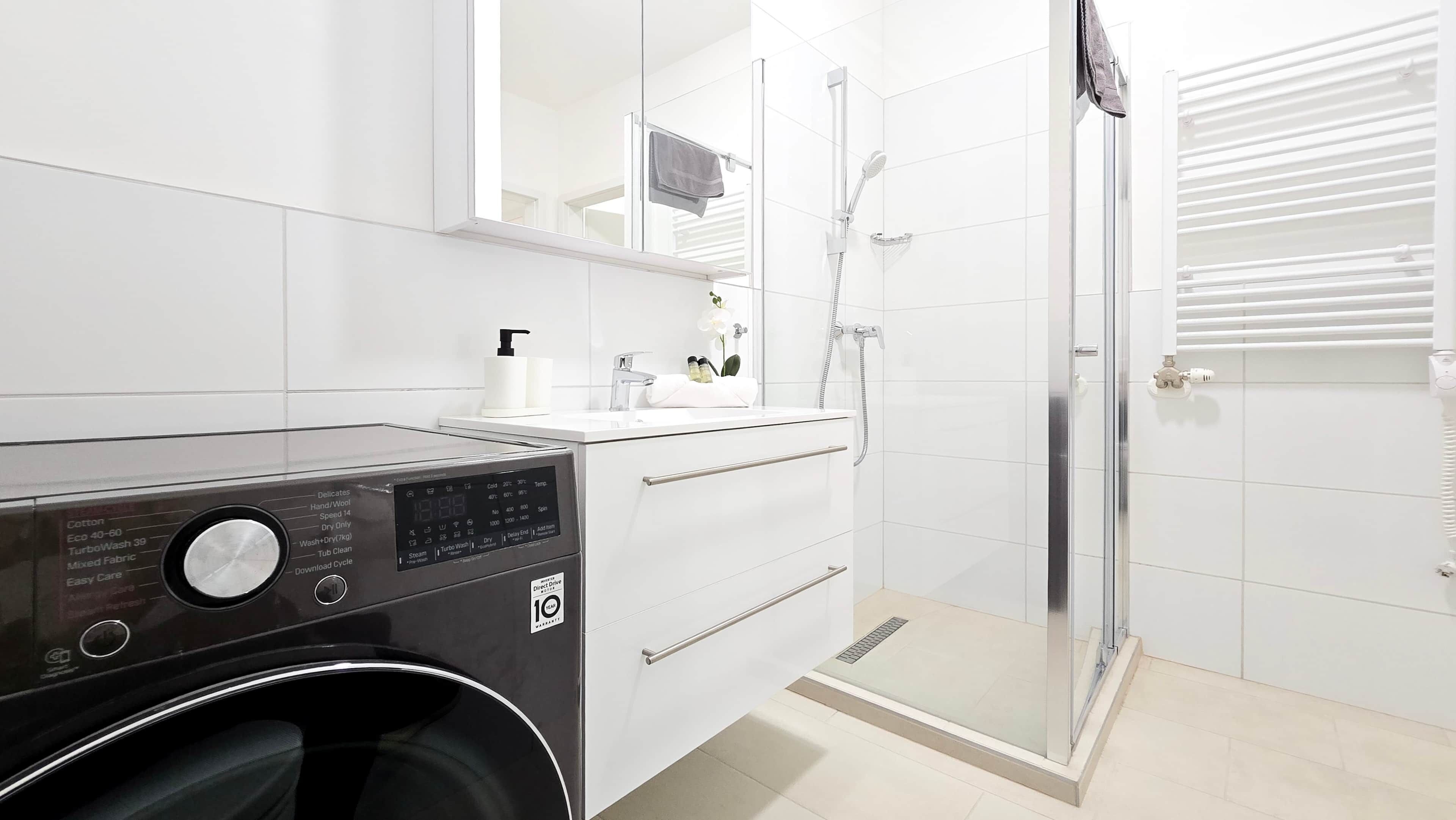 Un baño moderno con lavadora, lavamanos y ducha con cerramiento de vidrio.