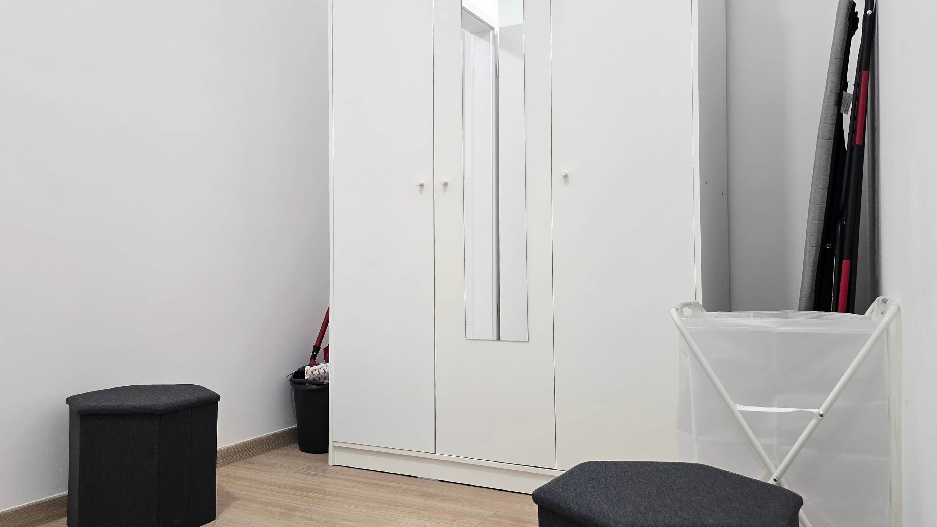 A room with a white wardrobe, a black trash bin, and a clear plastic storage unit.