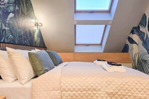 A bedroom with a bed, pillows, a headboard, a skylight, and a wall with a tropical leaf pattern. - IMCT - Urban Jungle Apartments 02 (Budapest)
