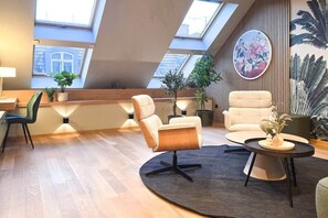A modern loft-style living room with skylights, a round coffee table, and a large plant. - IMCT - Urban Jungle Apartments 02 (Budapest)