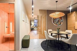 A modern interior with a dining area featuring a round table and chairs, a hanging light fixture, and a wooden wall with vertical slats. - IMCT - Urban Jungle Apartments 02 (Budapest)