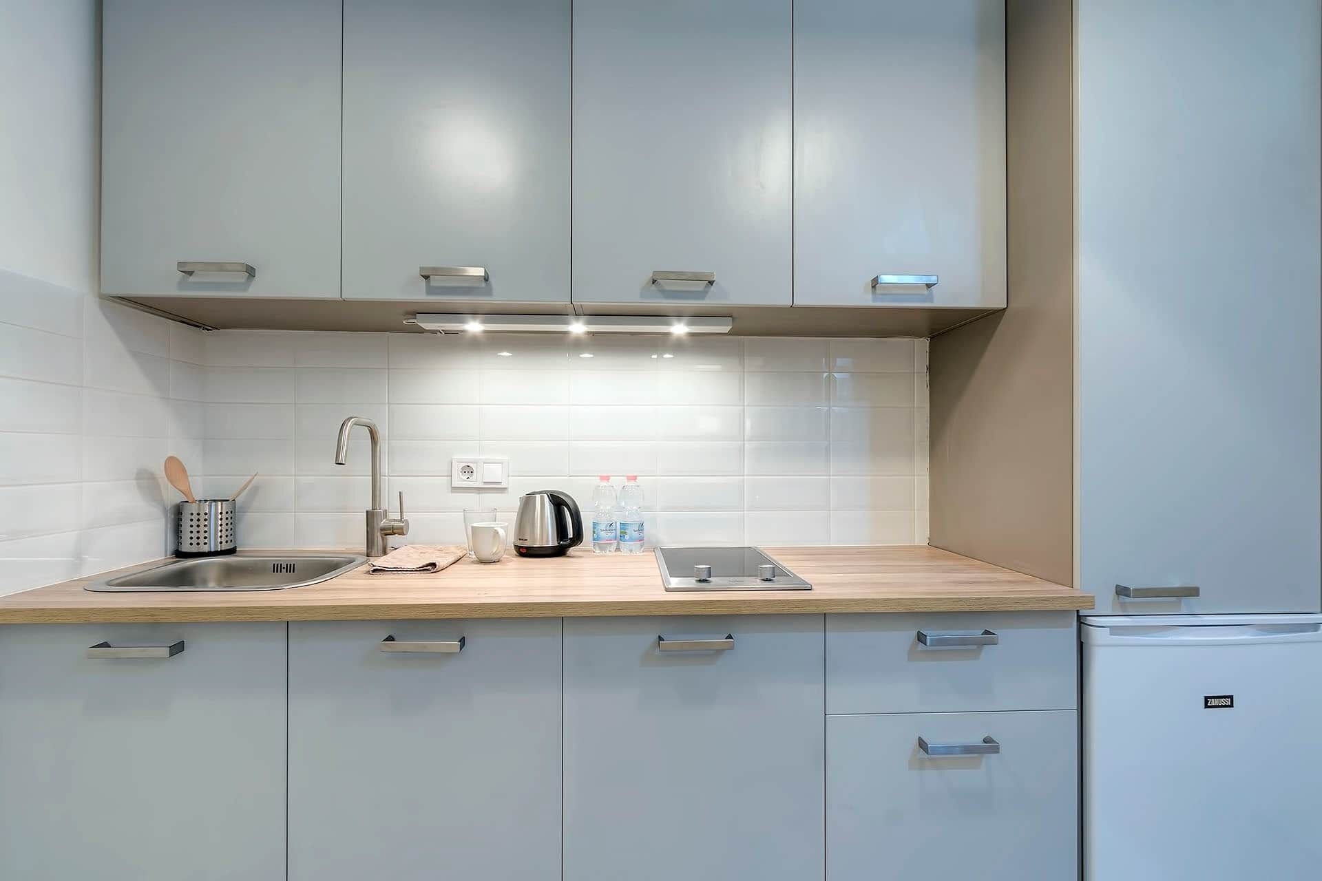 A modern kitchen with white cabinets, a stainless steel sink, and a built-in oven.