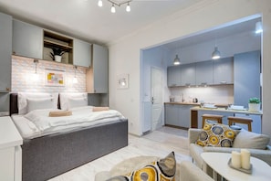 A modern hotel room with a bed, a sofa, a small table, and a kitchen area. - IMCT - Riverside Deluxe Apartment (Budapest)
