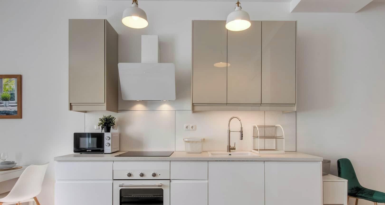A modern kitchen with a microwave, oven, and sink. There is a plant on the counter and a chair in the background.