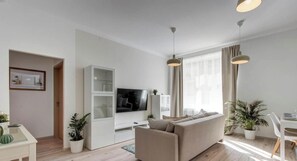 A modern living room with a sofa, TV, and dining area. - MidTerm - Rózsa Apartments - Arundhati (Budapest)