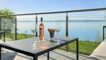 A table with a bottle and glasses on a balcony overlooking a lake.