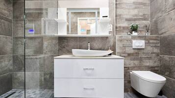 A modern bathroom with a glass shower enclosure, a white vanity with a vessel sink, and a toilet.