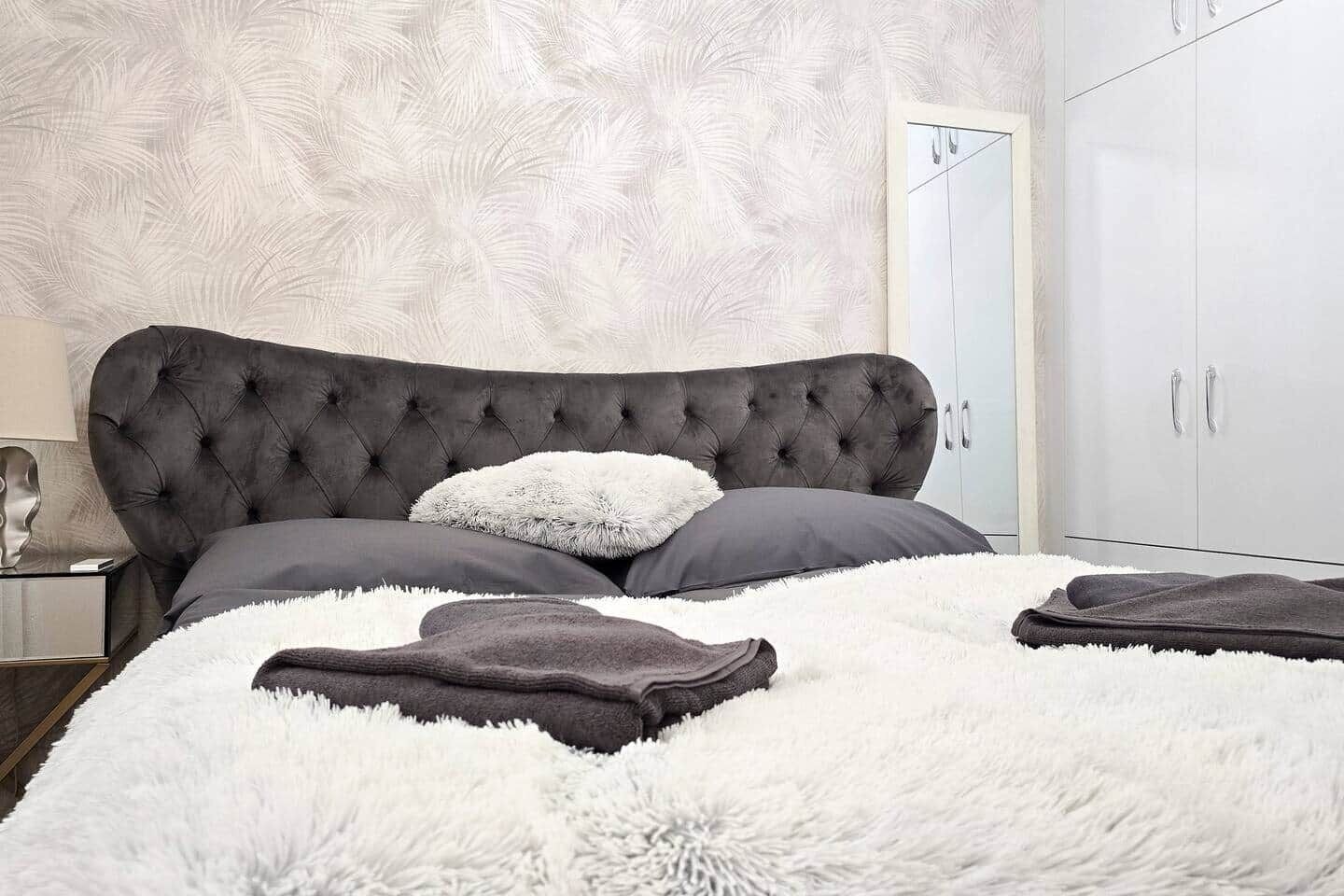 Una camera da letto con una testiera trapuntata, una coperta bianca e soffice e una coperta grigia.