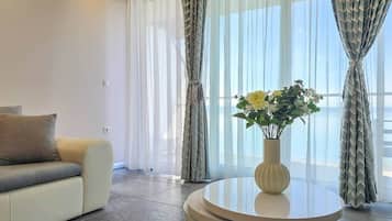 A living room with a sofa, a round table with a vase of flowers, and sheer curtains.
