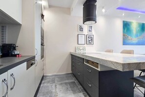 A modern kitchen with a central island, built-in appliances, and a painting on the wall. - LB - SunSet Panorama Apartment (Siófok)