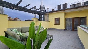 A rooftop terrace with a sofa, a table, and large green plants. - IMCT - Rooftop Serenity Apartment (Budapest)