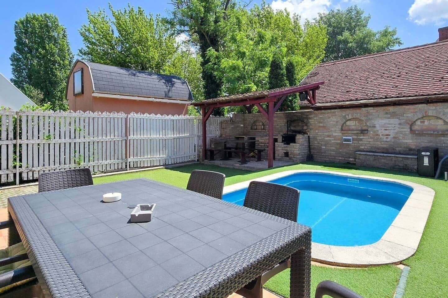 A backyard with a swimming pool, a covered patio area, and a stone building.