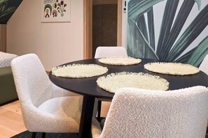 A dining area with a round table, white textured chairs, and woven placemats. - IMCT - Urban Jungle Apartments 10 (Budapest)