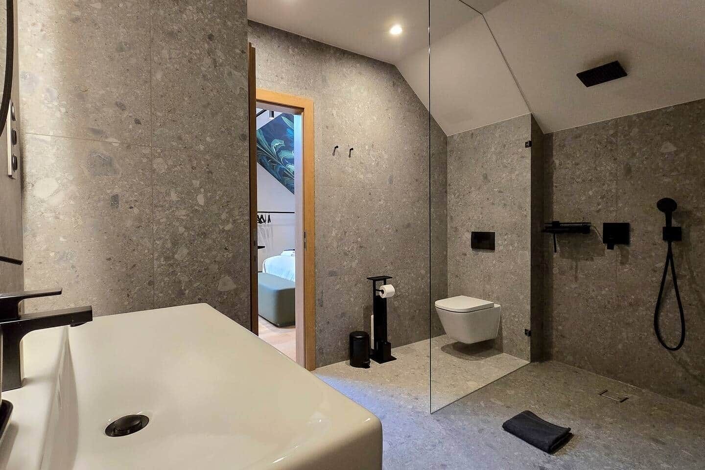 Un baño moderno con un lavamanos grande blanco, una ducha con cerramiento de vidrio y una habitación visible al fondo.