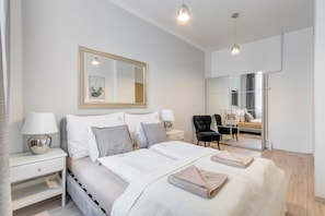 A modern bedroom with a large bed, bedside tables with lamps, a mirror, and a seating area with a chair and a sofa. - MidTerm - Rózsa Apartments - Daniel (Budapest)