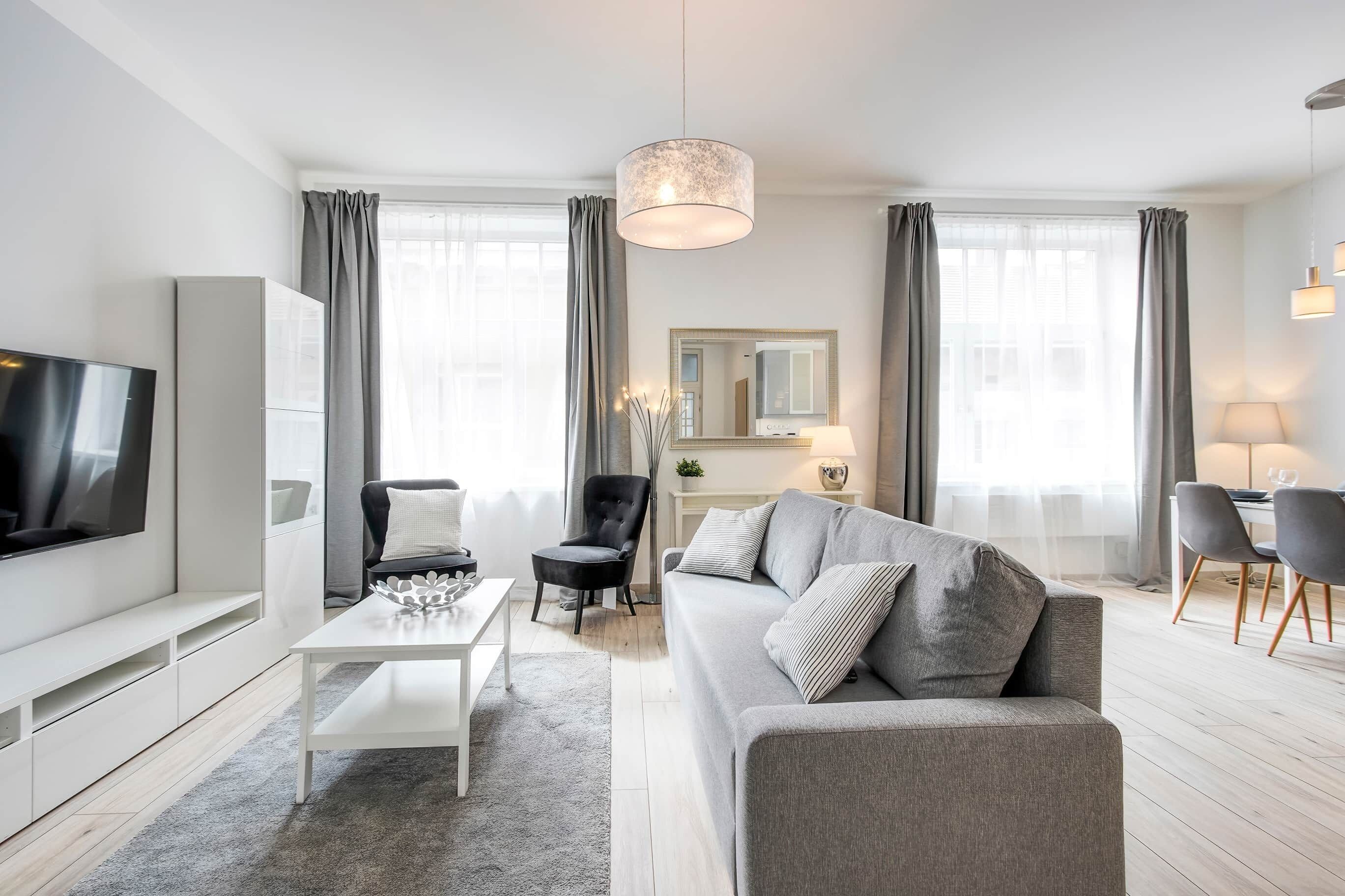 A modern living room with a grey sofa, a flat-screen TV, a coffee table, and a dining area with chairs and a table.