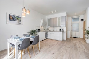 A modern kitchen with white cabinetry, a dining area with a table and chairs, and a potted plant on the wall. - MidTerm - Rózsa Apartments - Daniel (Budapest)