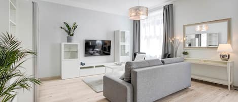 Una sala moderna con un sofá gris, un televisor de pantalla plana, una consola blanca y un espejo grande.