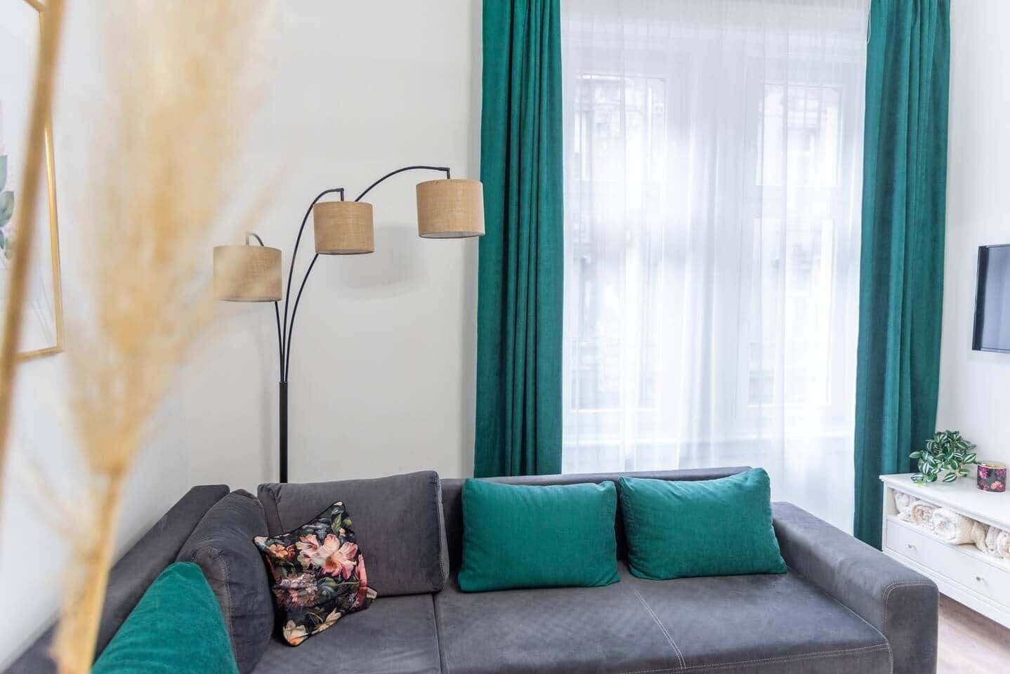 A living room with a grey sofa, teal cushions, a floor lamp, and a window with teal curtains.