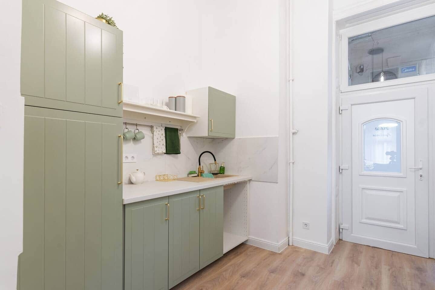 A kitchen with light green cabinets, a white countertop, and a window above the sink.