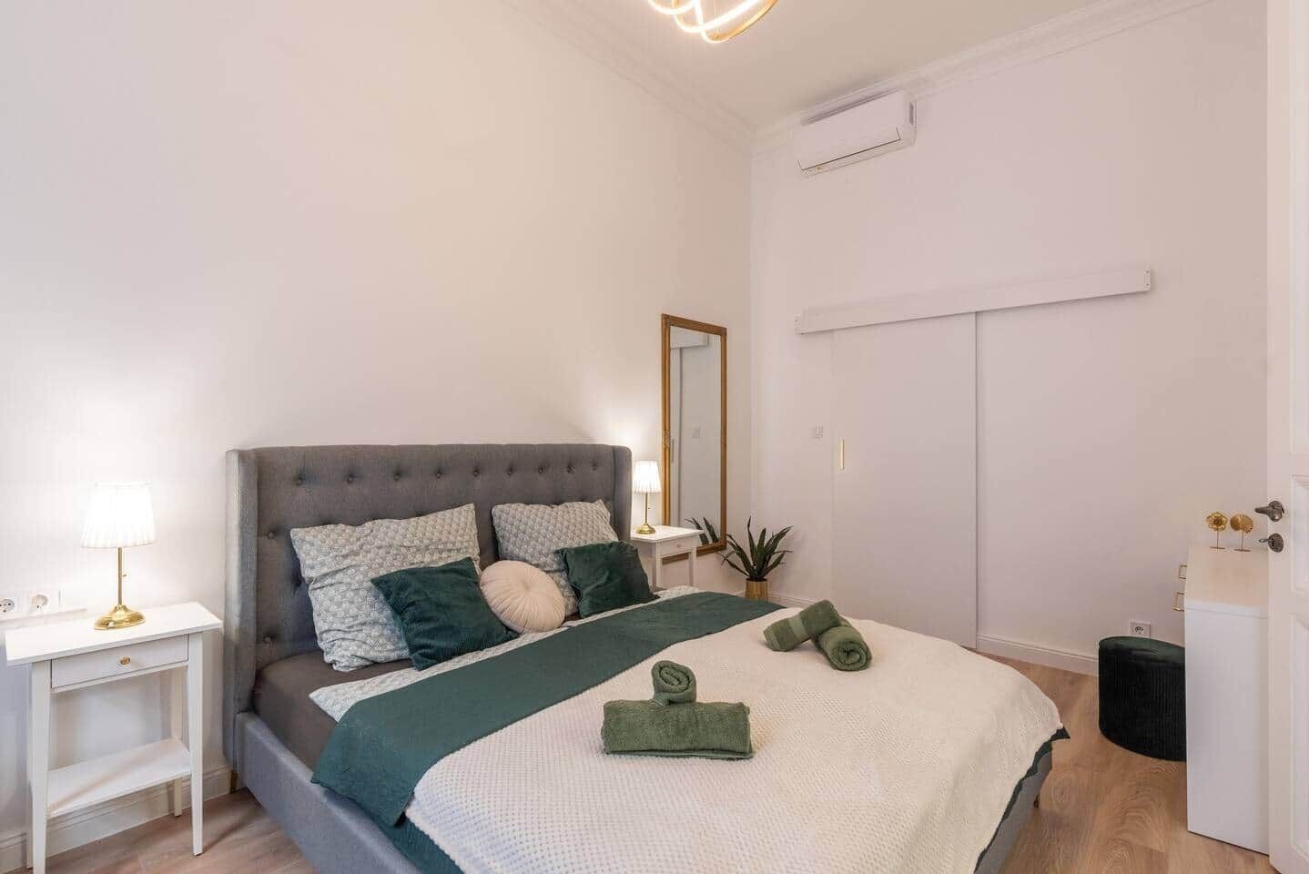 A neatly arranged bedroom with a bed, bedside tables, a mirror, and a wardrobe.