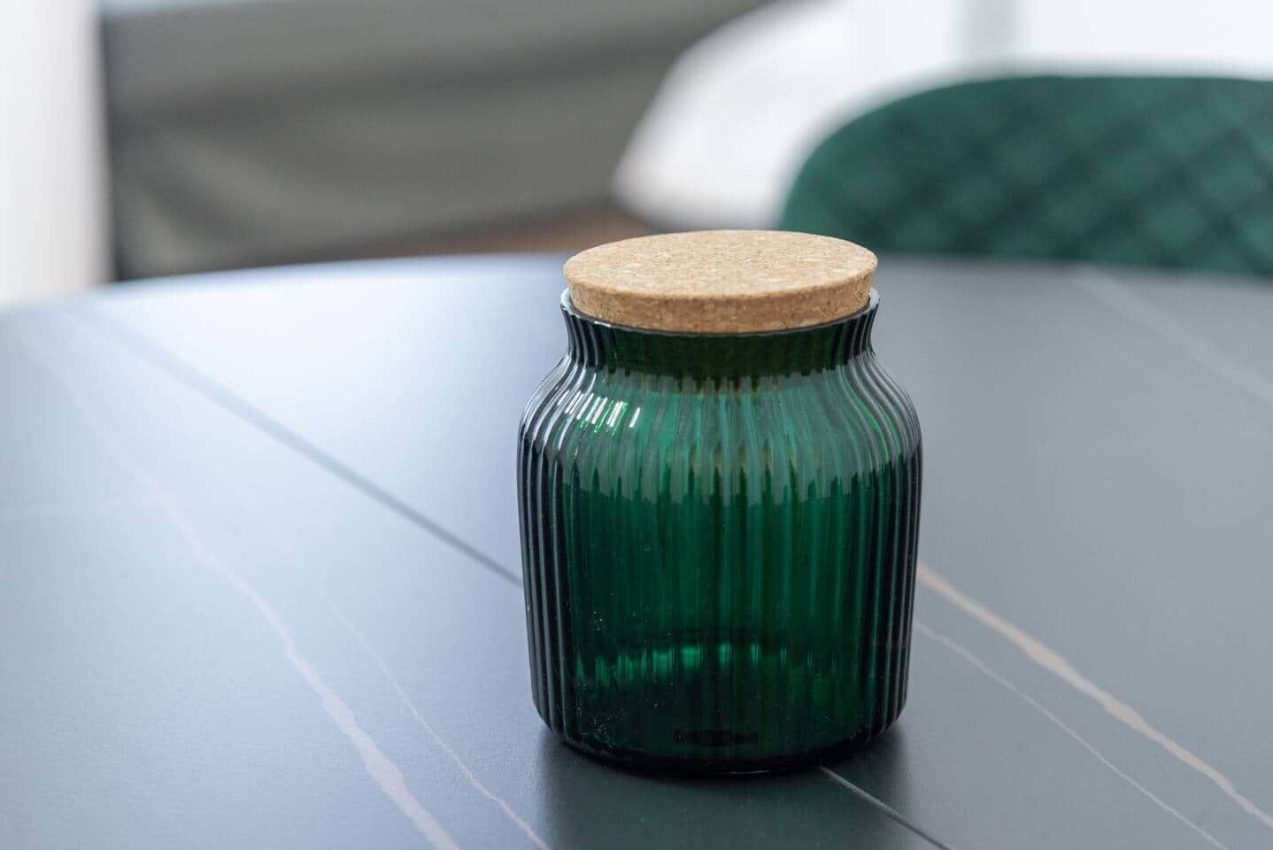 Un bocal en verre vert avec un couvercle en liège, posé sur une surface sombre.