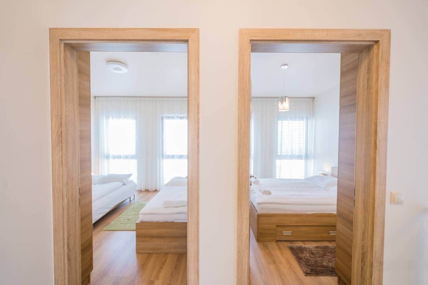 A hotel room with a wooden floor, a bed with white bedding, a bedside table, and a window with curtains.