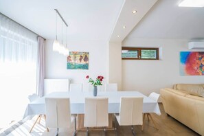 A modern living room with a dining area, featuring a white table, chairs, a beige sofa, and artwork on the walls. - LB - Silver Lodge 1 Siófok (Siófok)