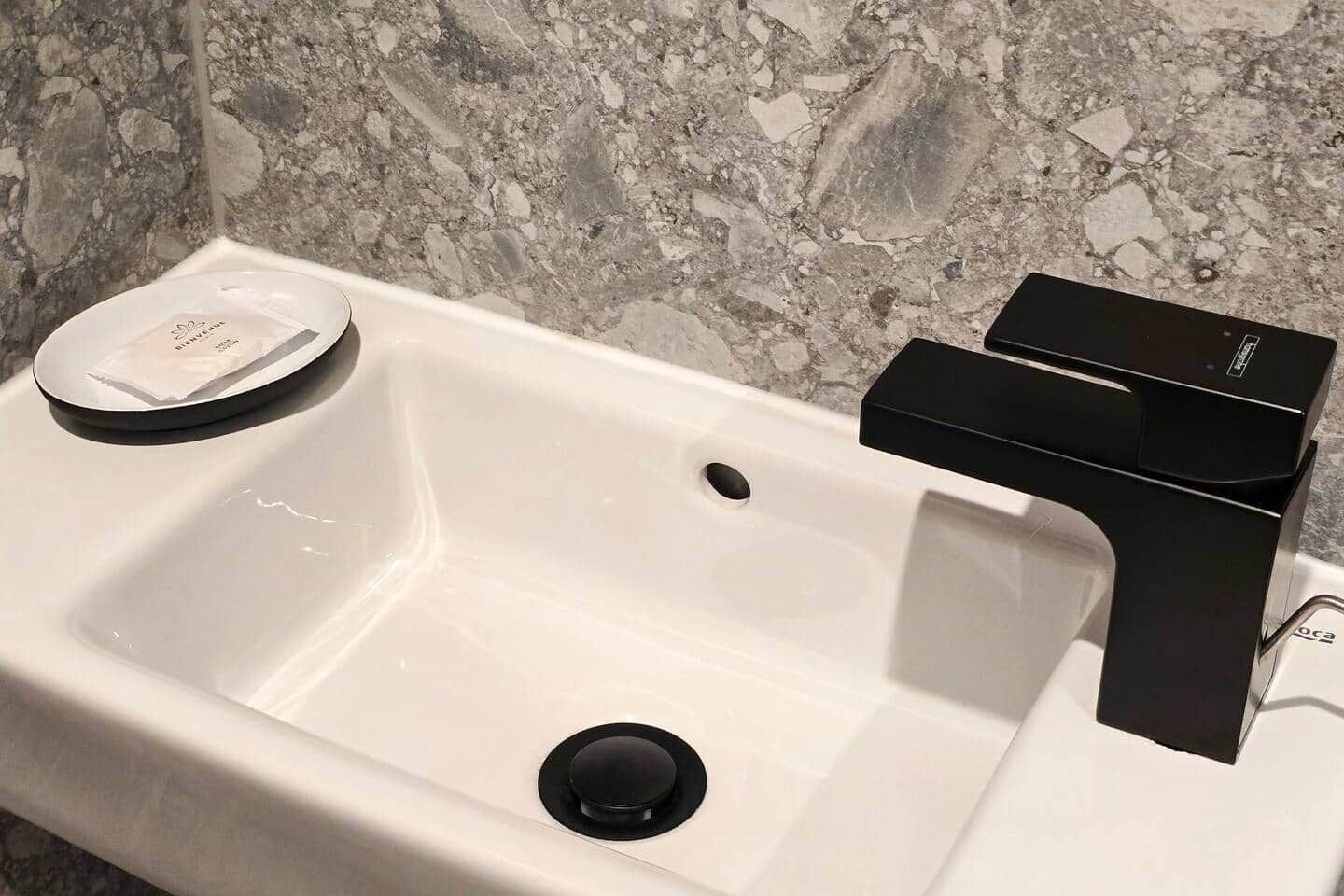 Een badkamer met een witte wastafel, een zwarte kraan en een zeepbakje.