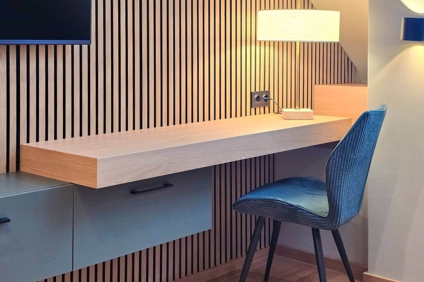 Ein modernes Zimmer mit integriertem Schreibtisch, einem Sessel, einem Flachbildfernseher und einer Lampe.