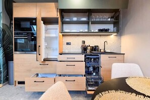 A compact kitchen with built-in appliances, open shelving, and a dishwasher. - IMCT - Urban Jungle Apartments 03 (Budapest)