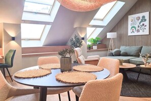 A modern interior with a round table, cushioned chairs, a sofa, and a large window. - IMCT - Urban Jungle Apartments 03 (Budapest)