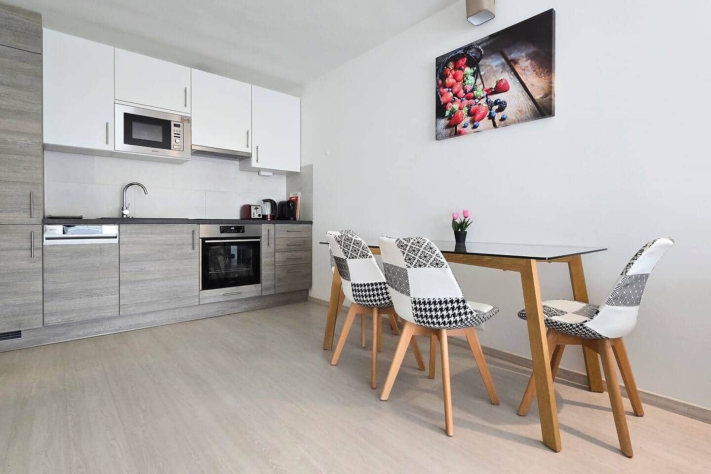 Una cocina moderna con armarios blancos, microondas y horno. Hay una mesa de comedor con cuatro sillas y un cuadro en la pared.