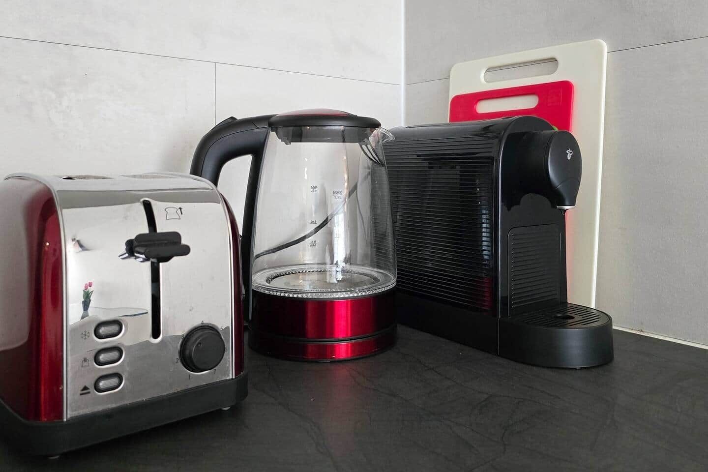 A kitchen with a toaster, a coffee maker, and a red and black appliance, possibly a rice cooker or slow cooker.