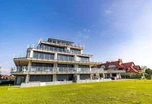 A multi-story hotel with a flat roof, large windows, and a grassy lawn in the foreground. - LB - LelleMarine Apartments A102 (Balatonlelle)