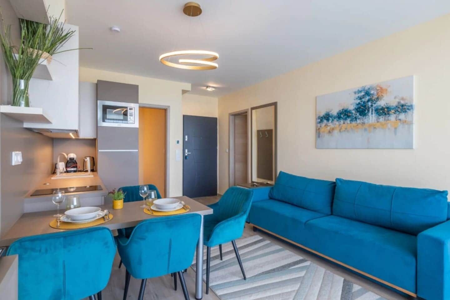Una sala de estar moderna con un sofá azul, una mesa de comedor con platos y vasos, y una zona de cocina con microondas.