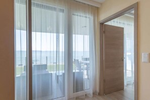 A room with a large sliding glass door leading to a balcony with a view of the sea. - LB - LelleMarine Apartments A102 (Balatonlelle)