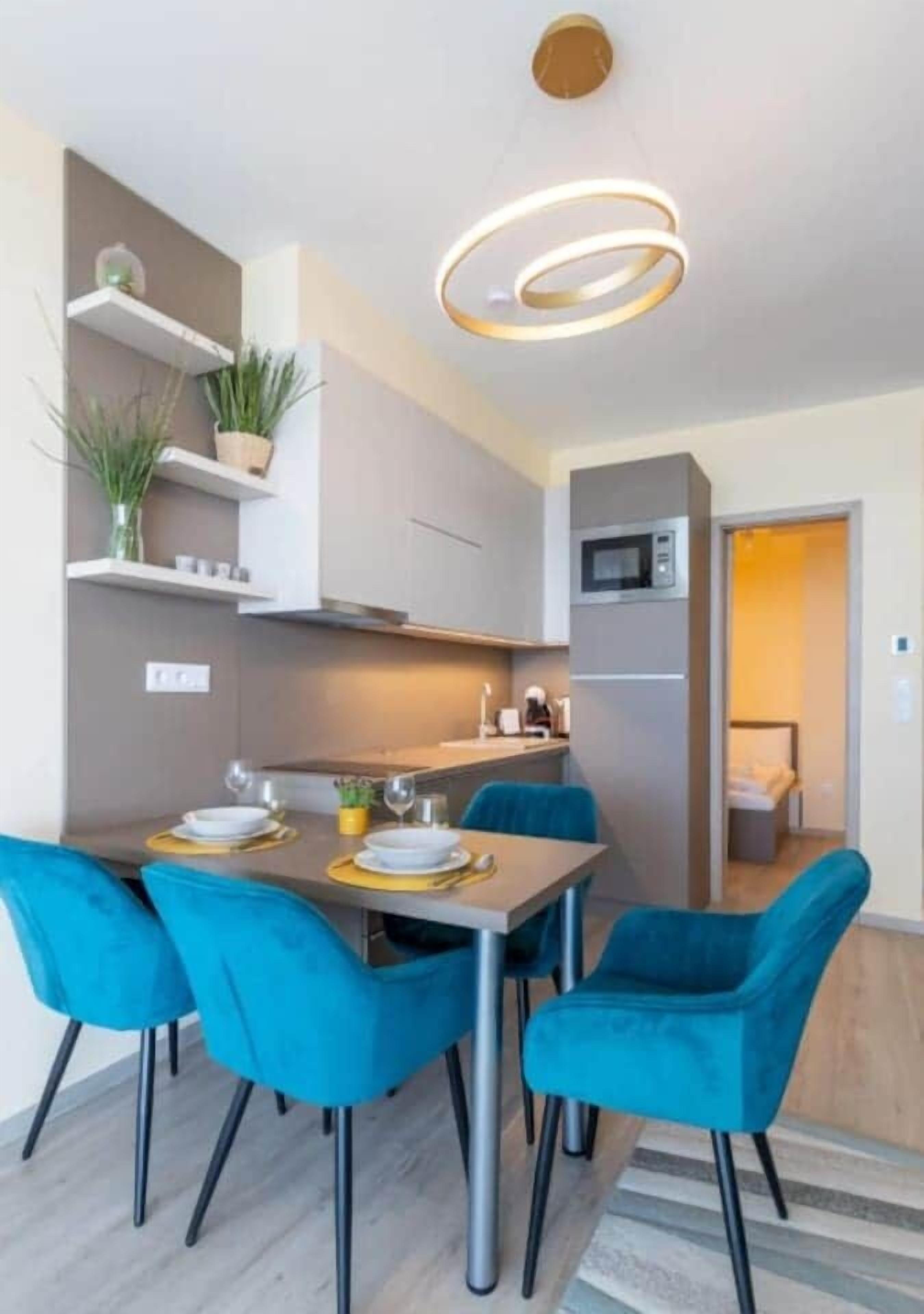 Een compacte keuken met moderne apparaten, een eettafel met stoelen en een plafondlamp.